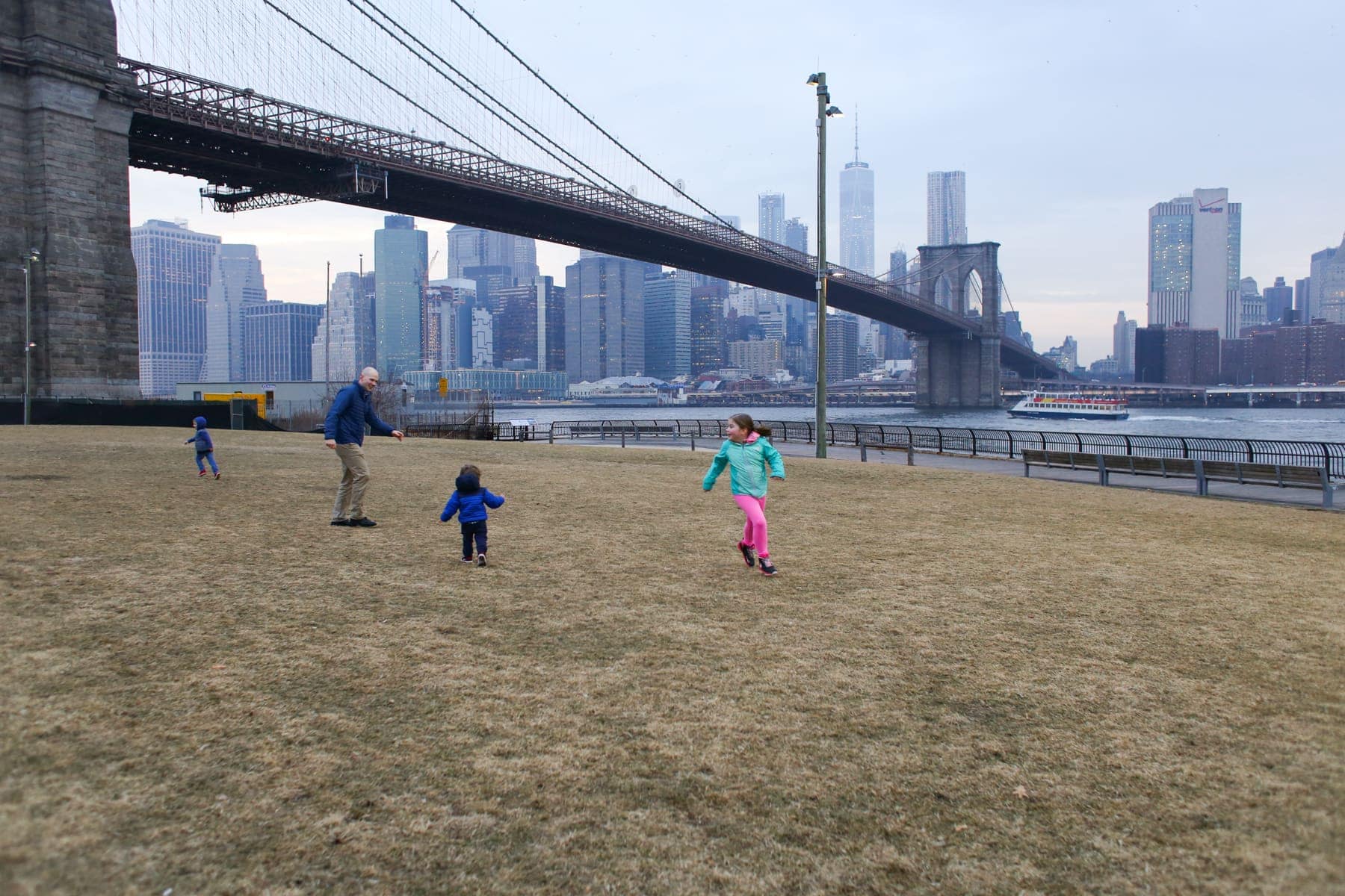 Brennan family playing in the grass with a bridge and city behind them