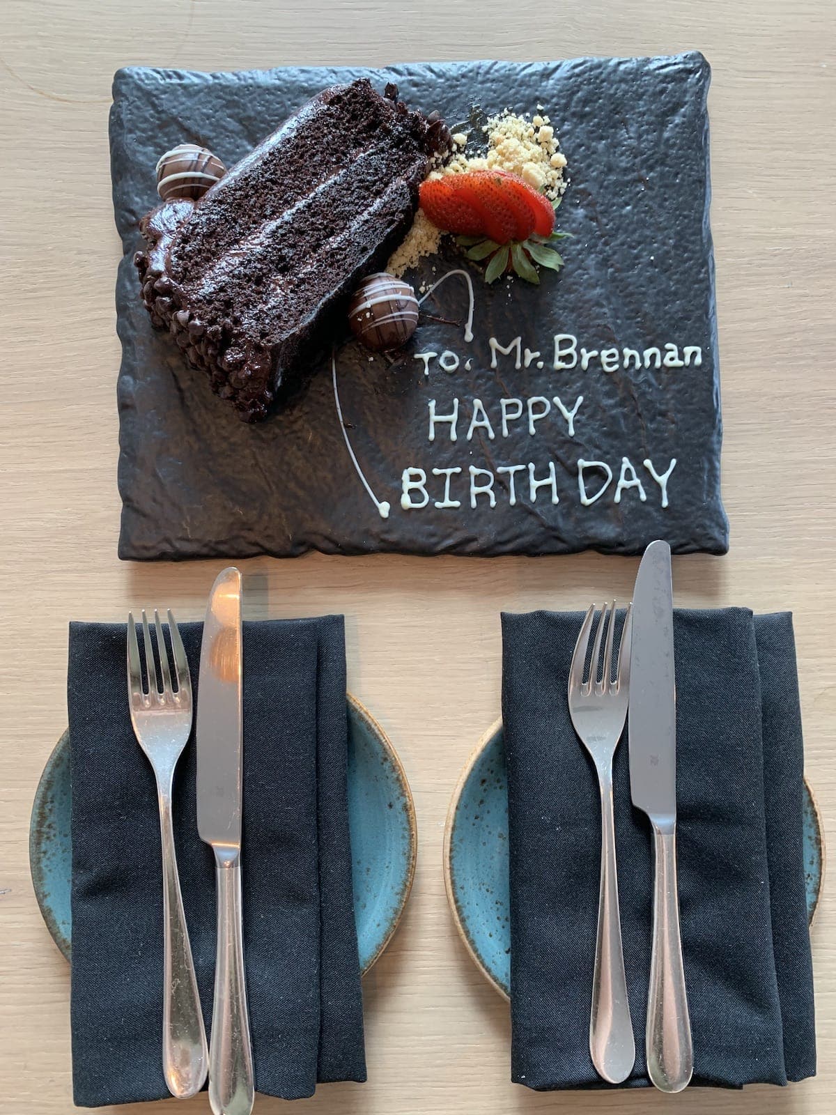 Chocolate cake on a slate plate with dinnerware in front.