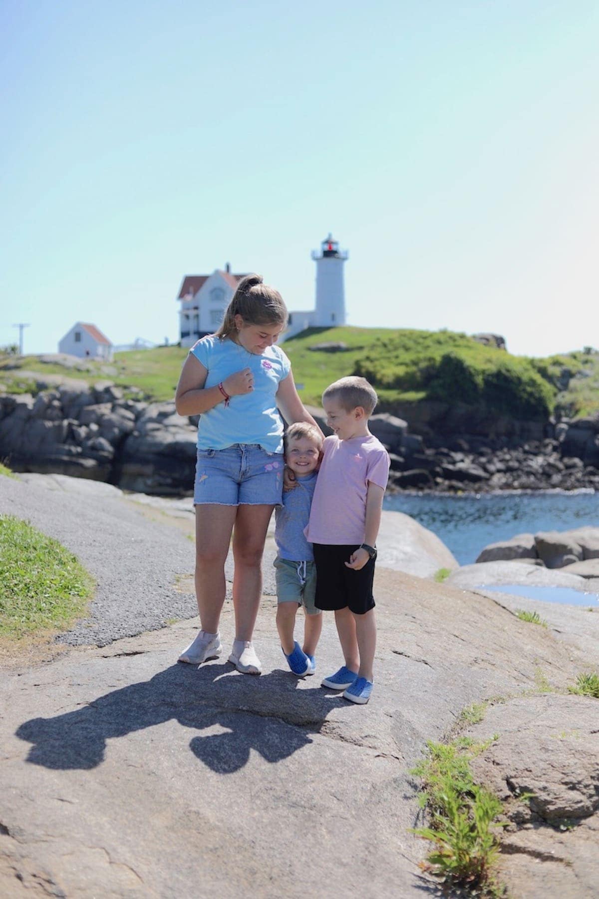 The kids standing on a rock with a light house in the background