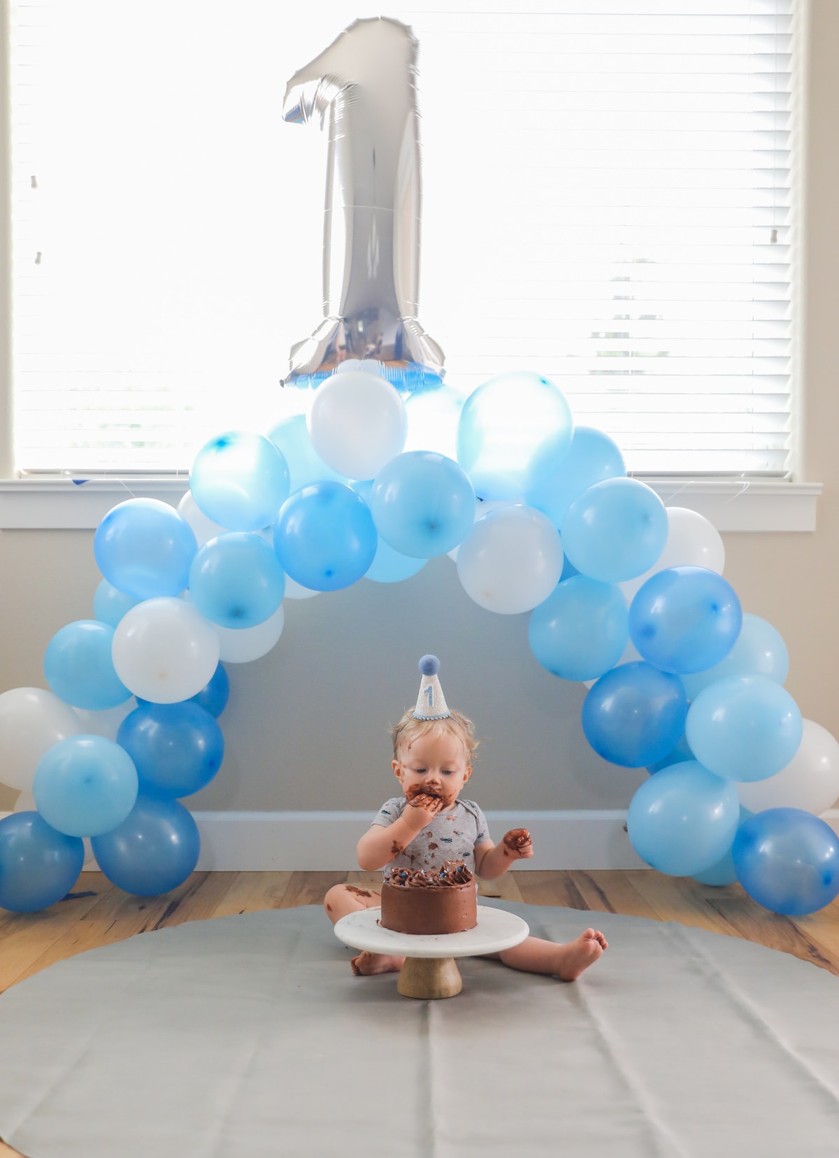baby sitting under ballon arch with cake